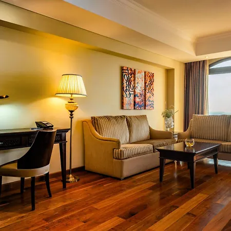 Pullman Resort Al Marjan Island Ras al-Khaimah Exterior photo The photo shows a cozy and stylish living area. It features two seating areas consisting of a light-colored sofa and a striped couch. There's a coffee table in the center made of dark wood. A desk with a lamp and a phone is positioned near the sofa. 